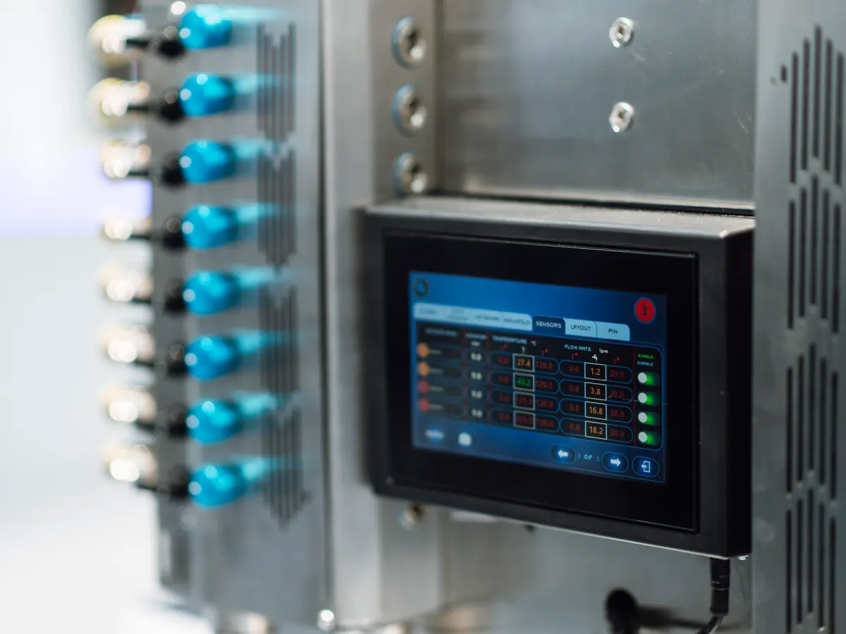 HMI touchscreen mounted on a machine control cabinet, showing sensor and flow-rate readouts
