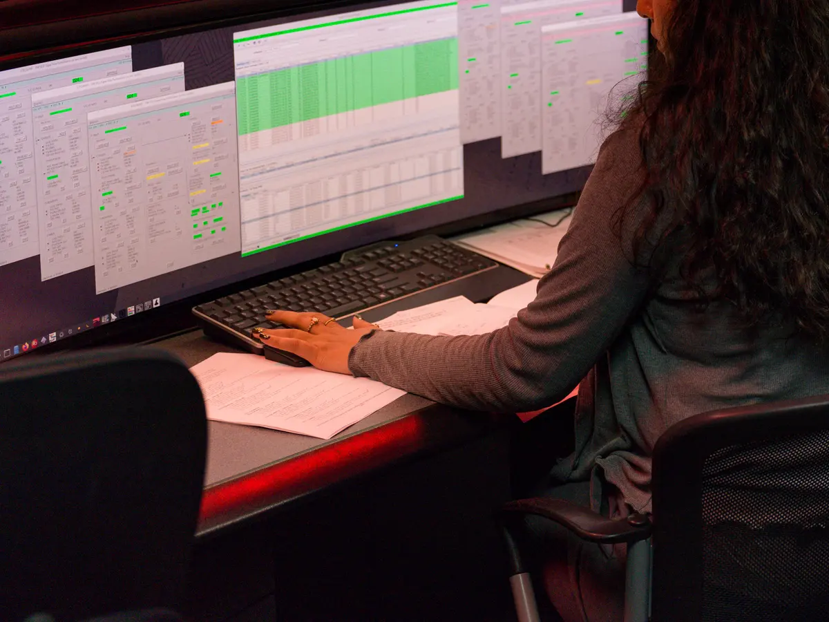 Analyst at a desk reviewing a data table on a monitor, rows highlighted green and yellow by status
